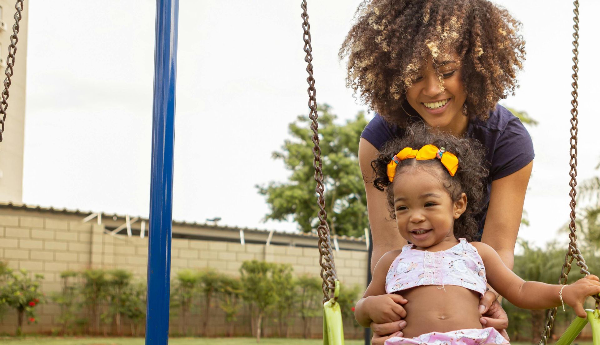 A happy mom pushes her daughter on a swing in a sunny playground, enjoying a beautiful day.