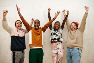A happy and diverse group of friends raising arms in excitement indoors.